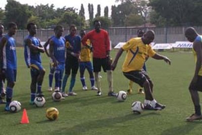 Jamhuri Kihwelu, dribbles as his players and his assistant Mohamed Ayoub (right) look on attentively during a training session.