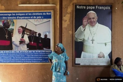 A woman stands in front of posters of Pope Francis at the Martyrs of Uganda church in Bamako, Mali.