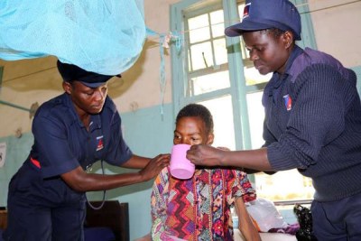 Security guards help a patient to drink porridge at her hospital bed at Kisumu County Hospital.